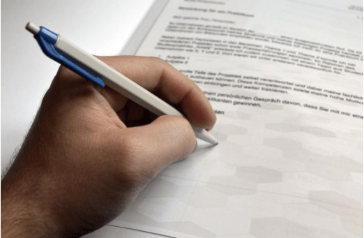 Bild einer Hand, die einen Stift hält und auf ein beschriebenes Blatt Papier unterschreibt